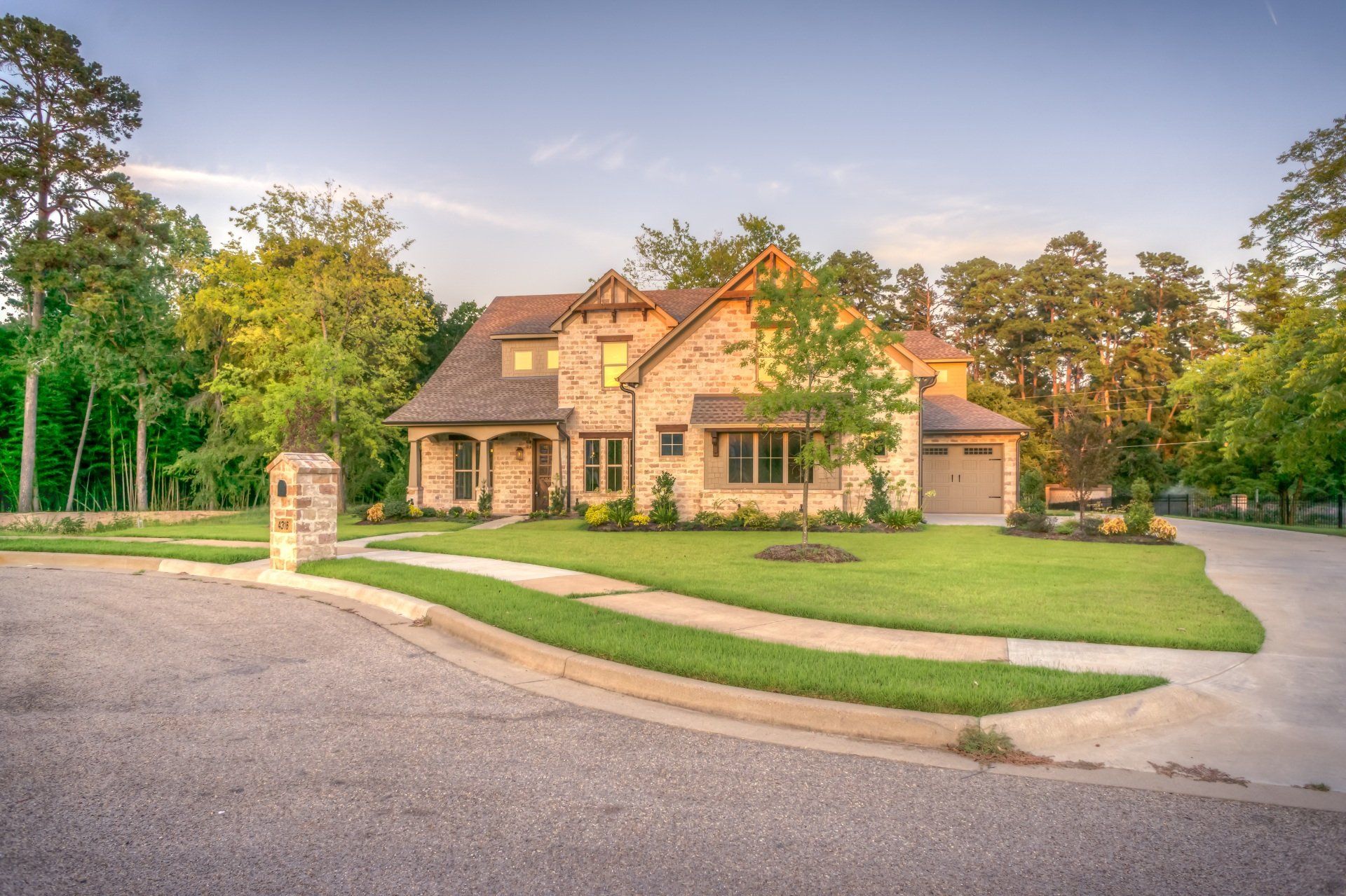 a large house with a lush green lawn is surrounded by trees and a driveway .